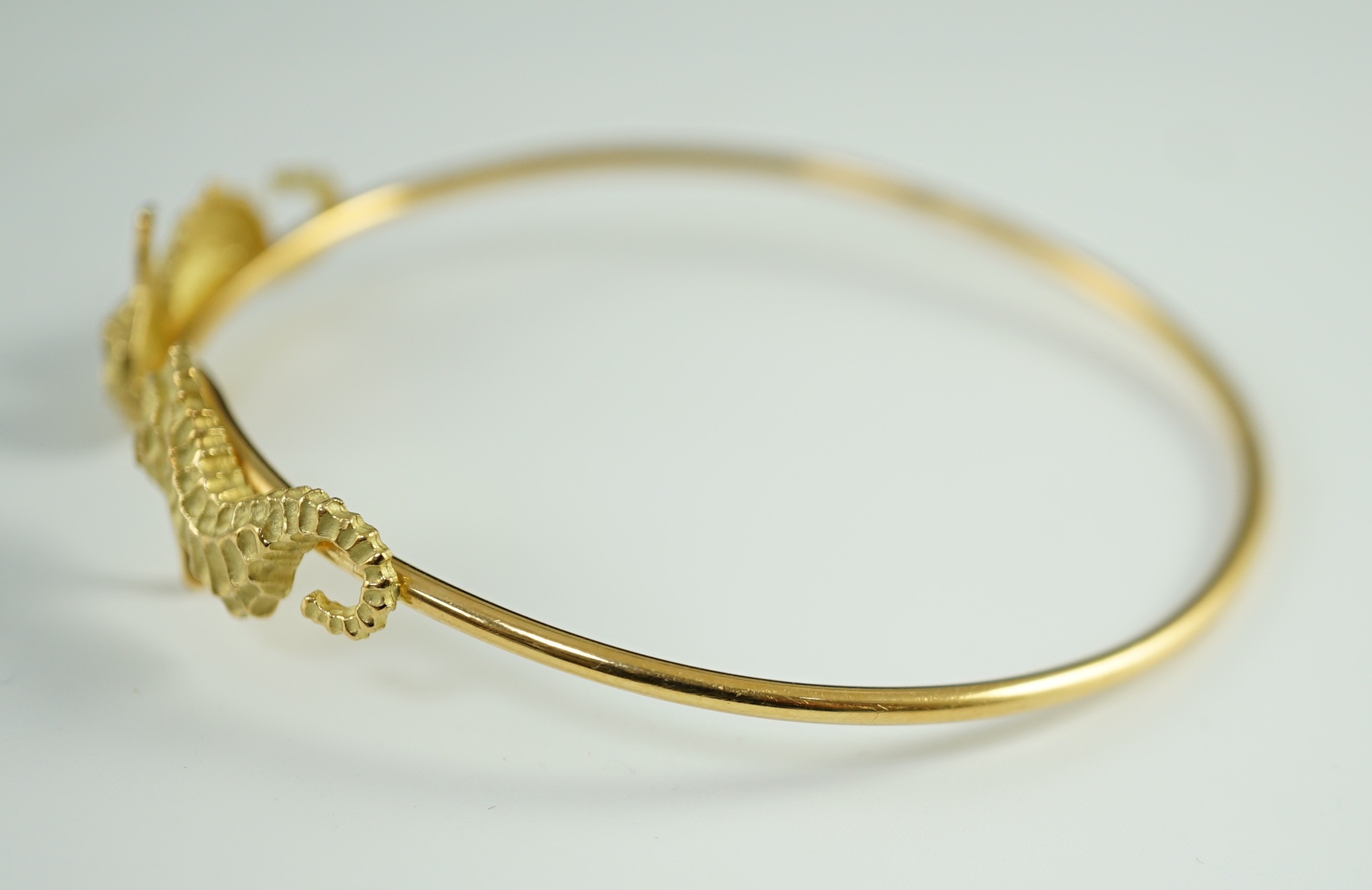 A modern gold and diamond chip set open work bangle, each terminal modelled as a seahorse with diamond chip eye